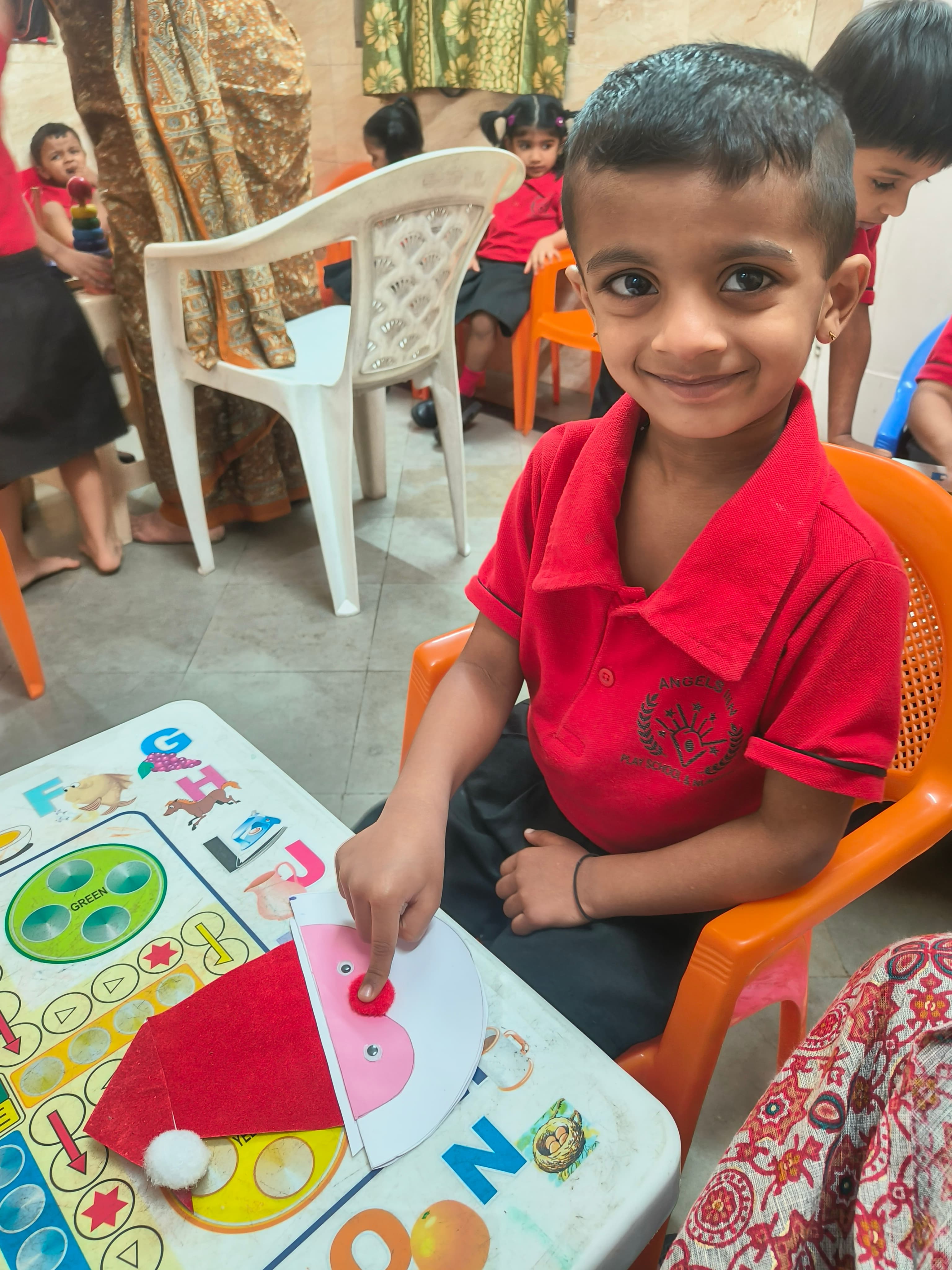 Boy in red school uniform making a red felt Santa hat craft at activity table